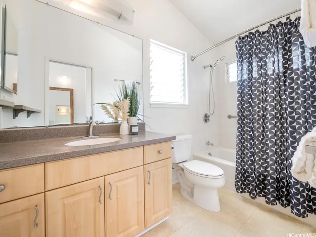 a bathroom with a granite countertop toilet a sink a mirror a shower and a window