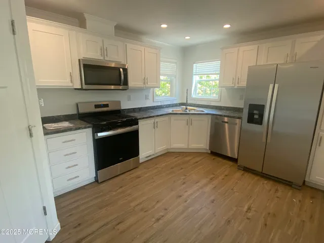 a kitchen with granite countertop a refrigerator stove a sink and dishwasher with wooden floor