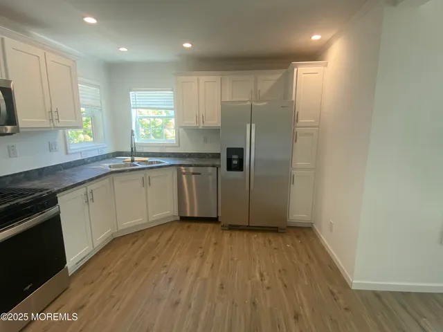a kitchen with stainless steel appliances granite countertop a refrigerator a sink and white cabinets with wooden floor