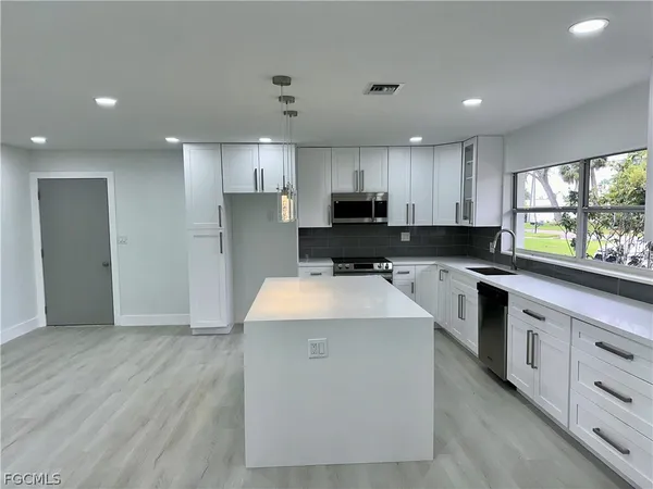 a large kitchen with stainless steel appliances kitchen island granite countertop a stove a sink a refrigerator and white cabinets with wooden floor