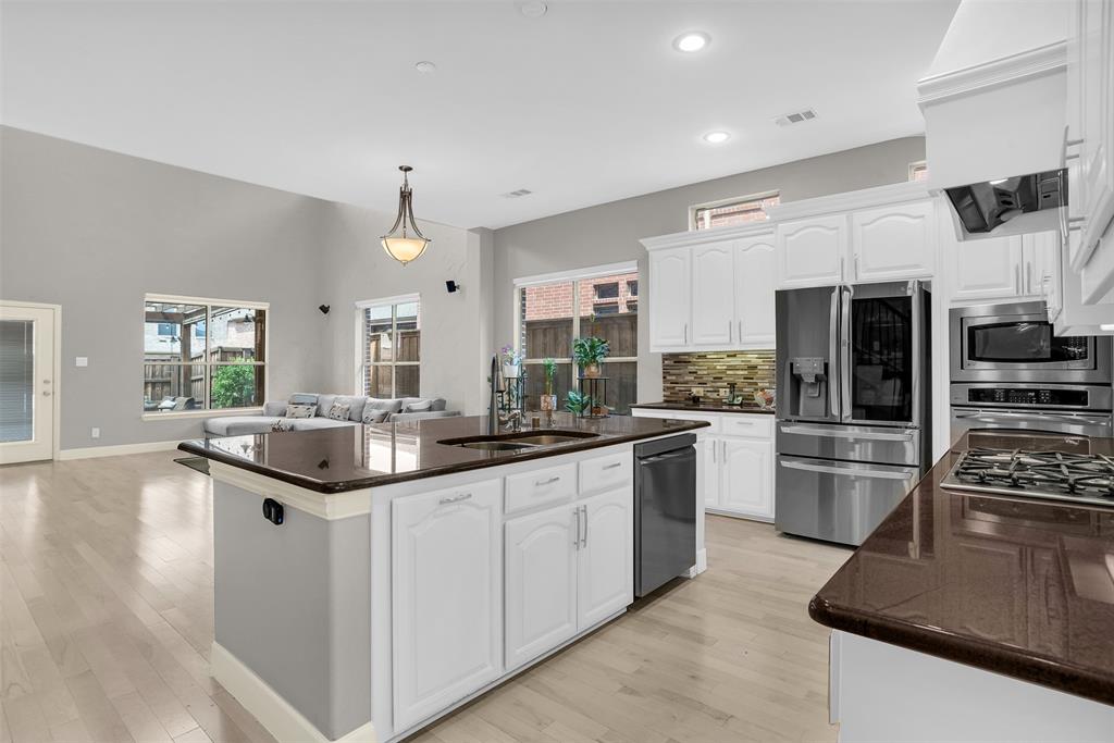 8631 Lohr Valley Road Irving, TX 75063 - Photo 30 of 32 Kitchen with white cabinetry, stainless steel appliances, open floor plan, decorative backsplash, and a kitchen island with sink