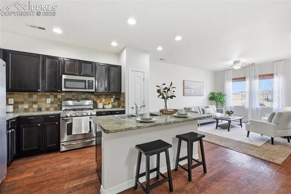 a kitchen with stainless steel appliances granite countertop wooden cabinets a stove a sink a dining table and chairs