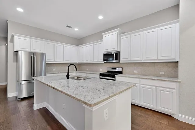 a kitchen with stainless steel appliances granite countertop a sink a stove a refrigerator and white cabinets