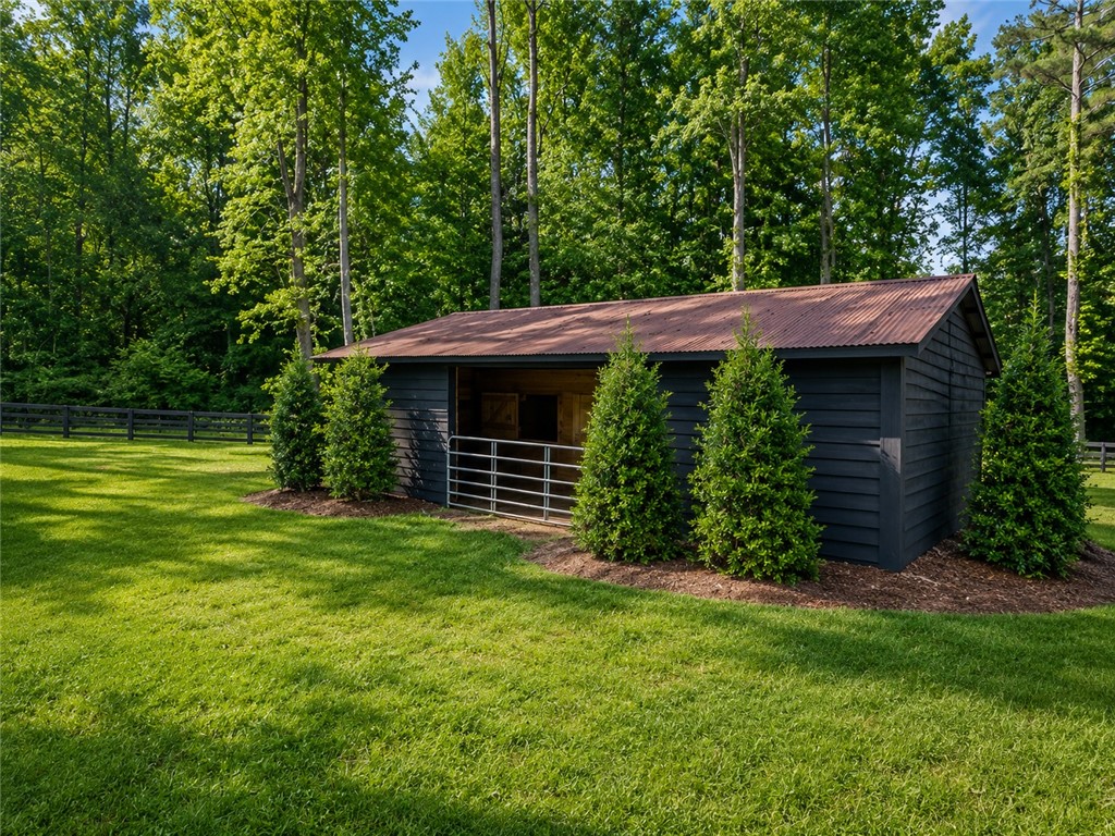 414 Devon Way Anderson, SC 29621 - Photo 45 of 50 A well-maintained stable and lush green pasture are framed by towering trees, offering an idyllic equestrian setting.