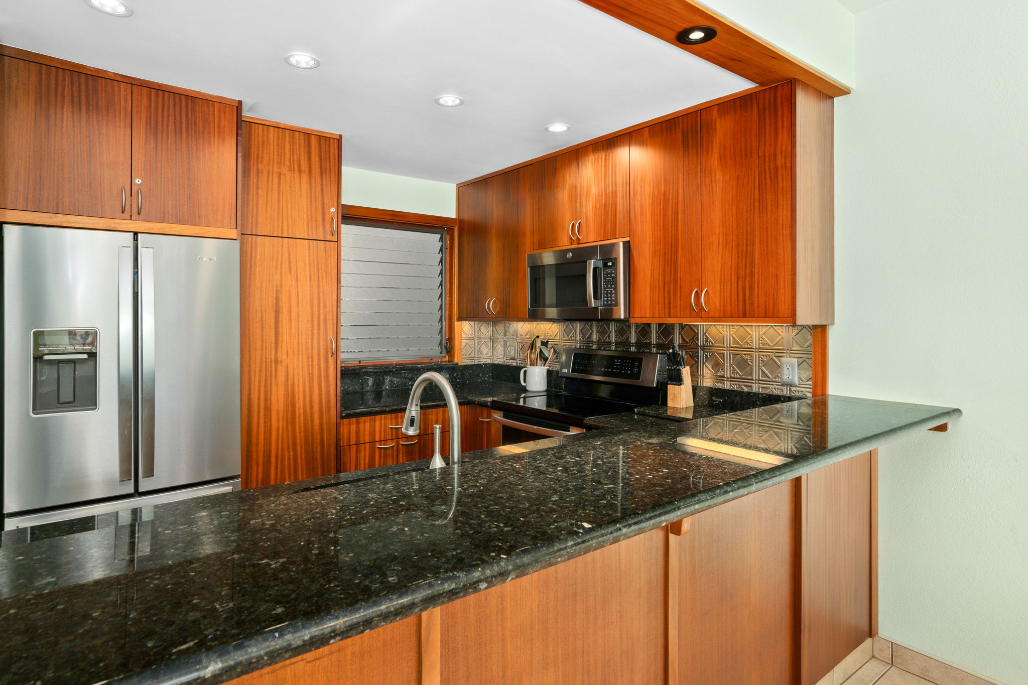 1568 Pe'e Road, Unit 211 Koloa, HI 96756 - Photo 8 of 30 a kitchen with stainless steel appliances granite countertop a refrigerator a stove and a sink with wooden floor