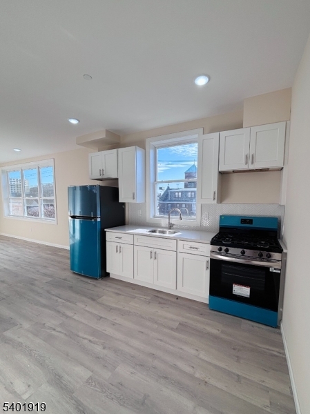 59 Cedar Street, Unit 303 Paterson, NJ 07501 - Photo 3 of 10 a kitchen with stainless steel appliances a stove a refrigerator a sink and white cabinets with wooden floor