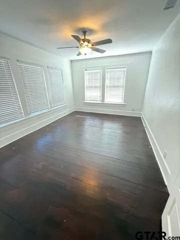 an empty room with wooden floor fan and windows