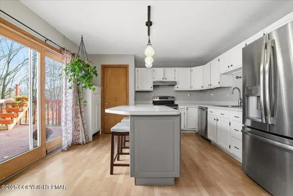 a kitchen with stainless steel appliances a stove a sink dishwasher a refrigerator white cabinets and wooden floor