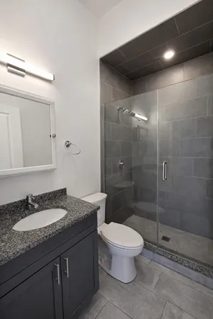 a bathroom with a granite countertop sink a toilet a mirror and shower