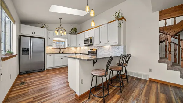 a kitchen with stainless steel appliances granite countertop a refrigerator a stove a sink dishwasher and white cabinets with wooden floor
