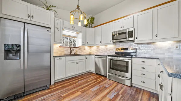 a kitchen with stainless steel appliances granite countertop a refrigerator a stove and white cabinets with wooden floors