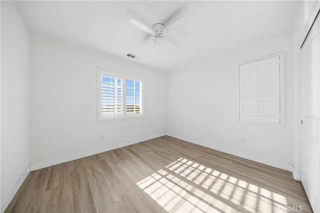 an empty room with wooden floor chandelier fan and windows
