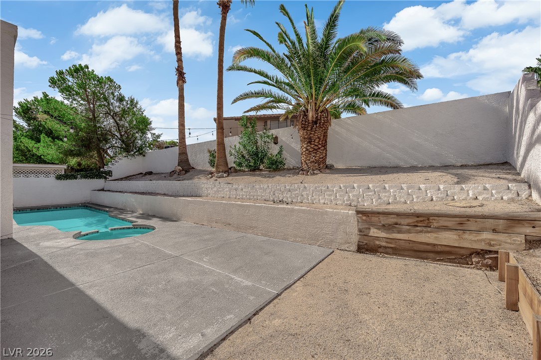 1433 Pathfinder Road Henderson, NV 89014 - Photo 28 of 35 A concrete patio borders the pool amidst tiered desert landscaping under a blue sky.