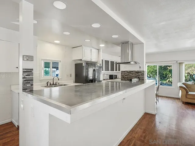 a large kitchen with kitchen island a large counter top stainless steel appliances a sink a window and cabinets