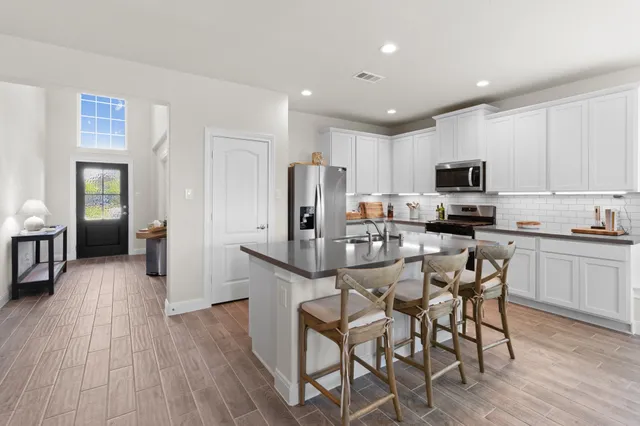 a kitchen with stainless steel appliances granite countertop a refrigerator a stove top oven a sink dishwasher and white cabinets with wooden floor