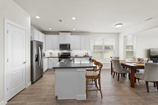 a kitchen with stainless steel appliances granite countertop a refrigerator a stove top oven a sink dishwasher a dining table and chairs with wooden floor