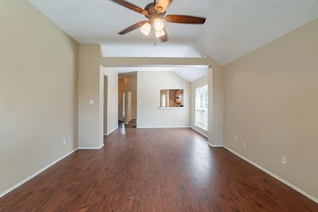 an empty room with wooden floor chandelier fan and windows