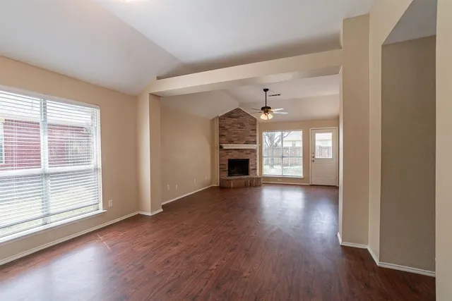 an empty room with wooden floor fireplace and windows