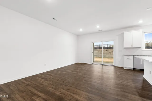 a view of empty room with wooden floor and kitchen