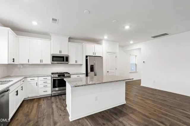 a large kitchen with stainless steel appliances granite countertop a stove a sink and white cabinets with wooden floor