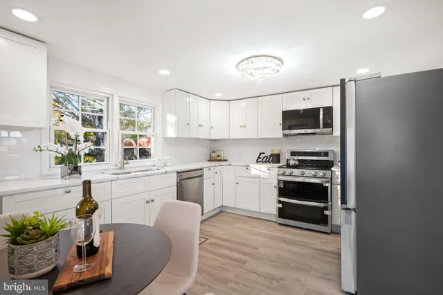 a kitchen with stainless steel appliances a stove a sink dishwasher a refrigerator and a dining table with wooden floor