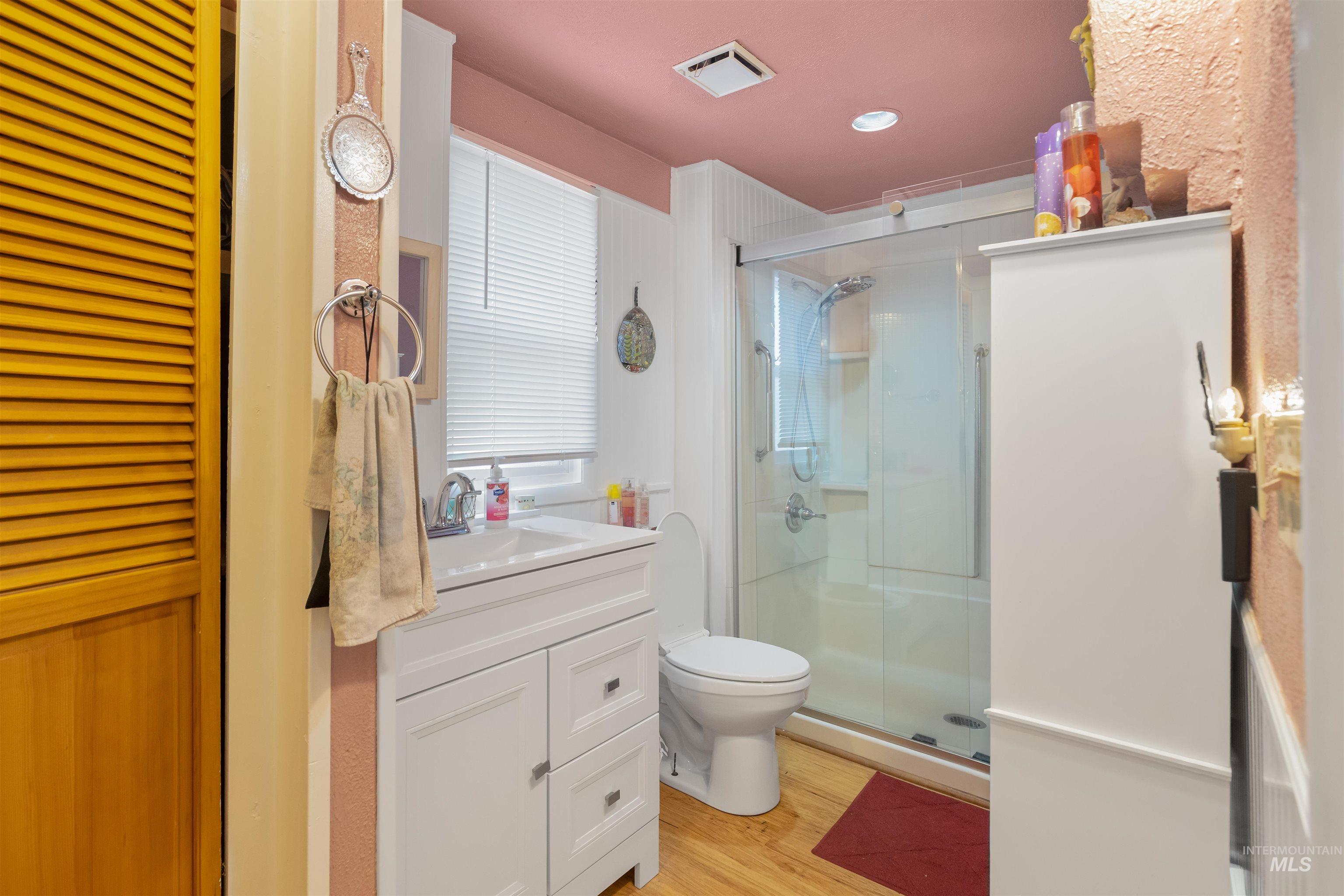 238 Hillcrest Road Lewiston, ID 83501 - Photo 22 of 27 Bathroom featuring a white vanity with integrated sink, chrome faucet, glass-enclosed shower, light wood-finish flooring, and a louvered bifold door