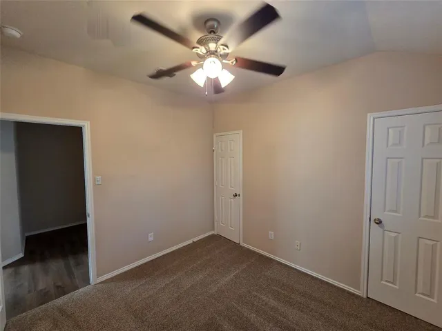 an empty room with a chandelier fan and wooden floor