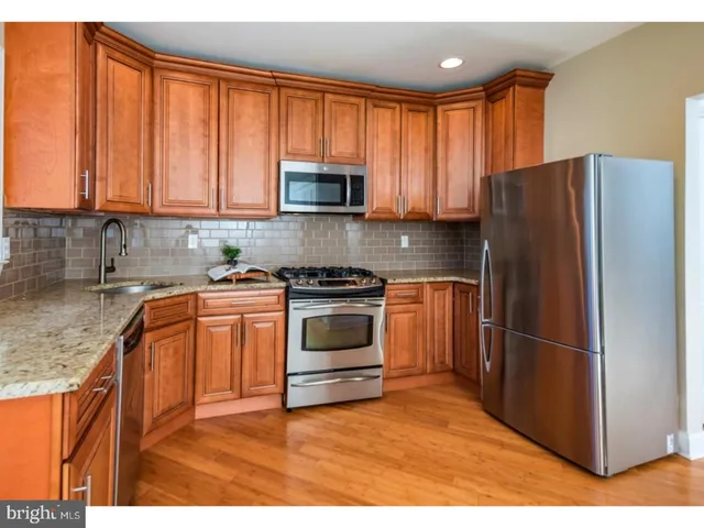 a kitchen with granite countertop wooden cabinets a stove a refrigerator and a sink