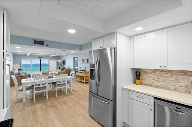 a kitchen with stainless steel appliances granite countertop a refrigerator a sink dishwasher a dining table and chairs with wooden floor