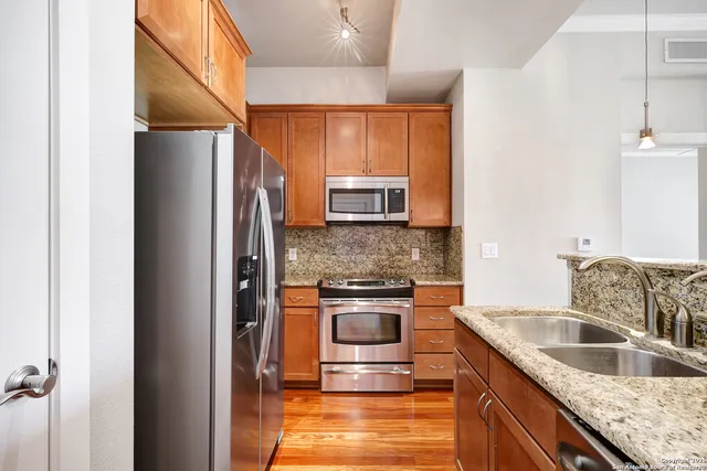 a kitchen with stainless steel appliances granite countertop a refrigerator a stove and a sink with wooden floor