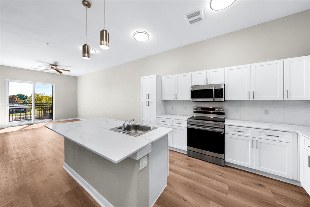 3522 Main Street, Unit 203 Rowlett, TX 75088 - Photo 6 of 20 a kitchen with stainless steel appliances a stove a sink dishwasher a refrigerator white cabinets and wooden floor