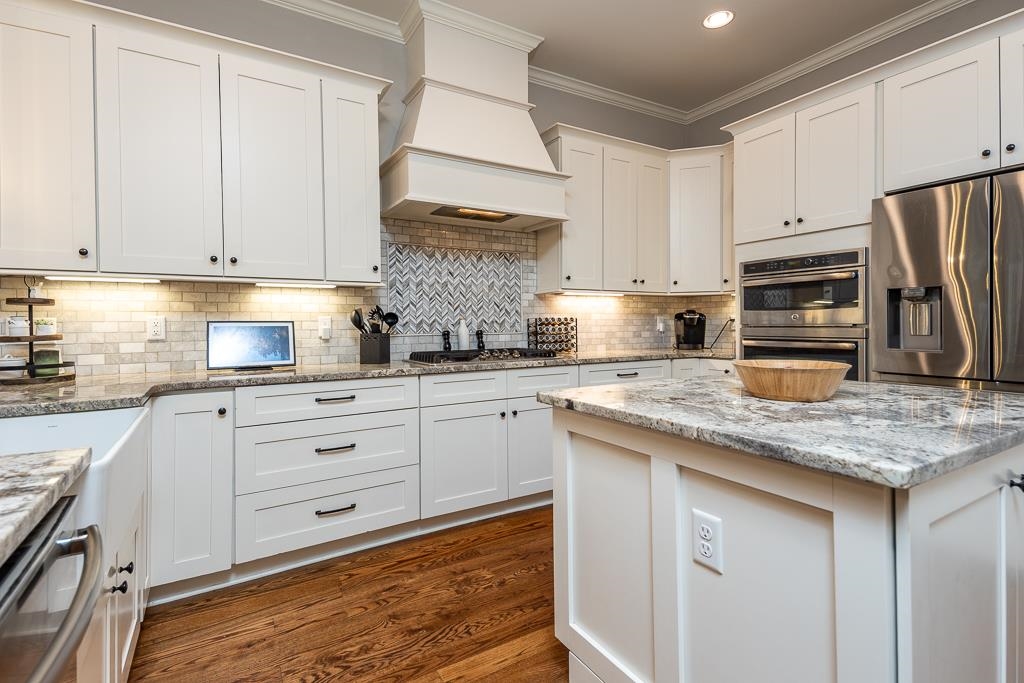 328 Washington Street Collierville, TN 38017 - Photo 10 of 33 Kitchen featuring white shaker cabinetry, an island with a stone countertop, a tile backsplash, wood-finish flooring, and stainless steel appliances