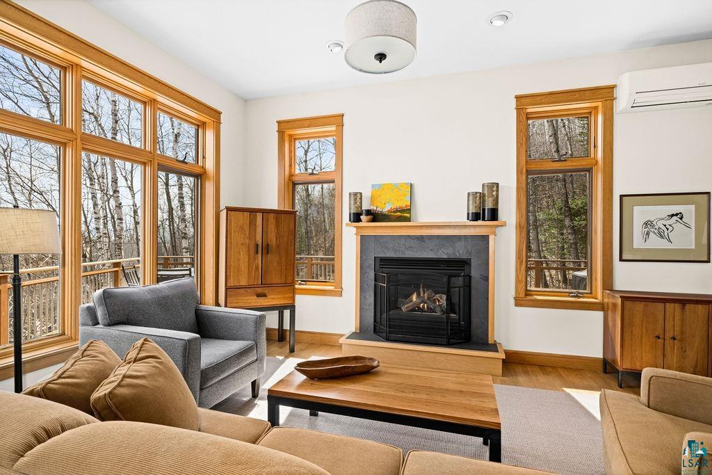 4856 Kingston Street Duluth, MN 55804 - Photo 4 of 88 Living space featuring a stone-surround fireplace, light wood-finish flooring, natural wood window trim, and a wall of floor-to-ceiling windows