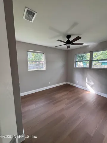 an empty room with wooden floor fan and windows