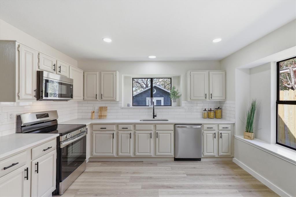 3405 Mill Ridge Street Bedford, TX 76021 - Photo 3 of 32 Contemporary kitchen featuring light wood-finish flooring, white cabinetry with black hardware, stainless steel appliances, and a white subway tile backsplash