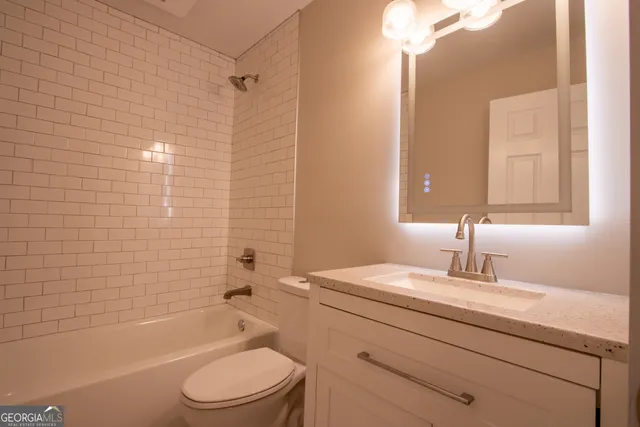 a bathroom with a granite countertop toilet a sink a mirror a bathtub and shower