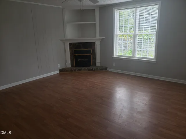 an empty room with wooden floor fireplace and windows