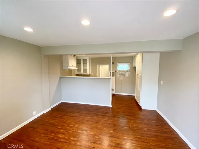 a view of empty room with wooden floor and kitchen view