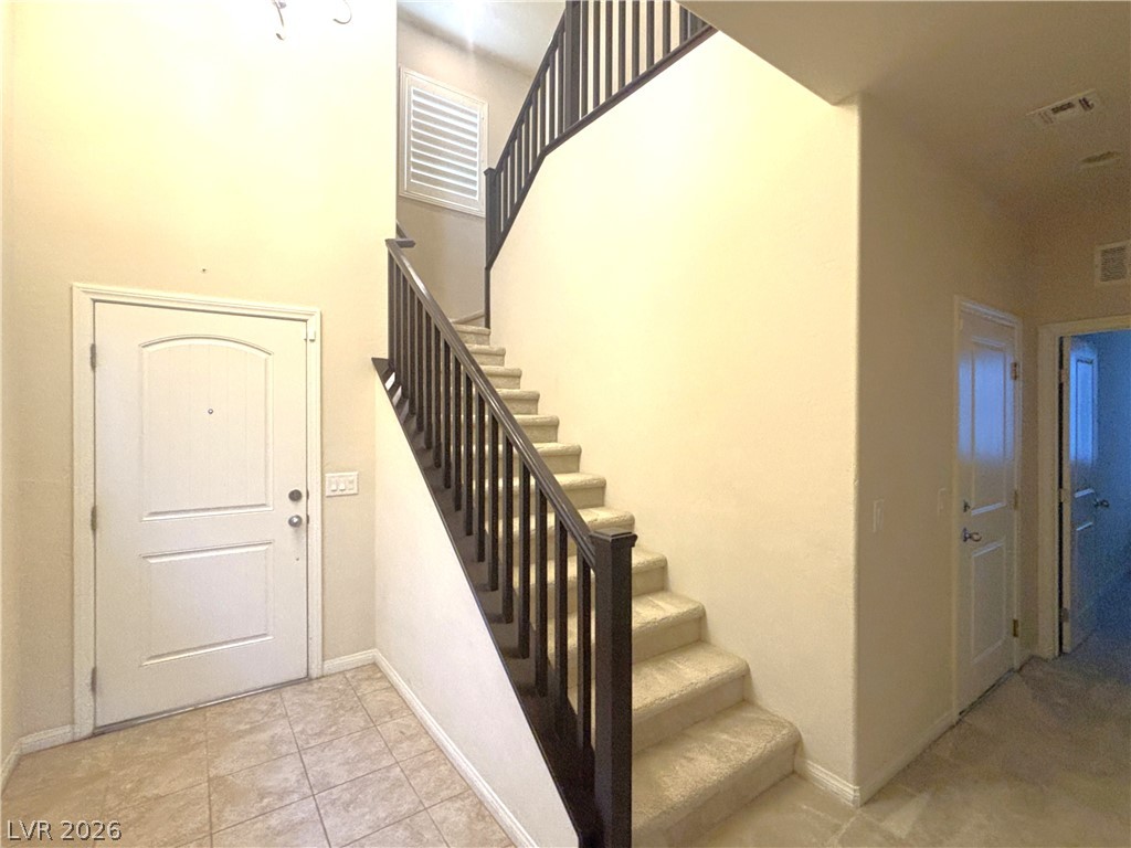 121 Elm Reed Avenue Las Vegas, NV 89113 - Photo 5 of 30 A graceful staircase with dark wood railings ascends from a tiled entryway, inviting exploration.