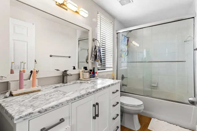 a bathroom with a granite countertop bathtub shower sink mirror and toilet