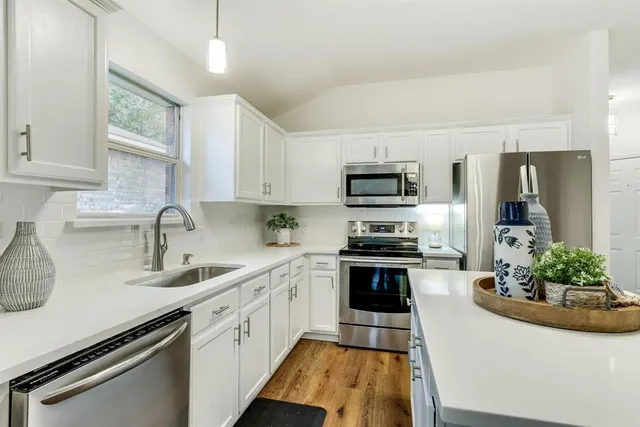 a kitchen with stainless steel appliances white cabinets a sink a stove a refrigerator and microwave