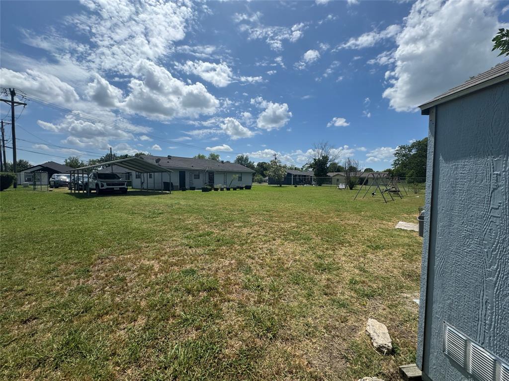 207 College Mound Road Terrell, TX 75160 - Photo 11 of 14 Expansive grassy yard featuring a detached storage shed with vertical siding, a metal carport, and a single-story residence with a dark shingle roof