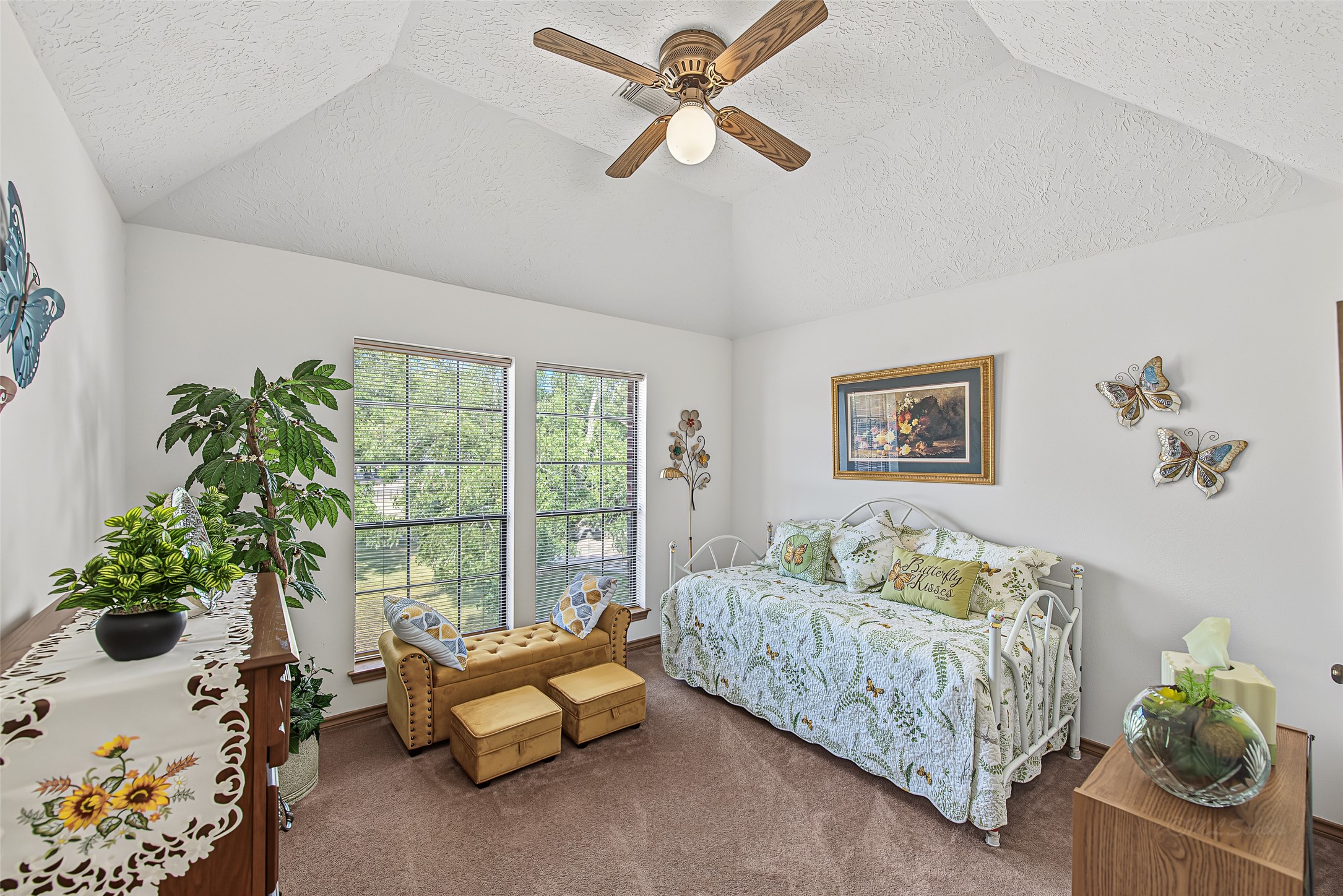 1345 Peach Ridge Road Brookshire, TX 77423 - Photo 35 of 50 This charming secondary bedroom features a vaulted tray ceiling with a central ceiling fan that enhances the room's sense of height and open space. Twin floor-to-ceiling windows flood the area with natural light while providing serene views of the surrounding tree-lined property.