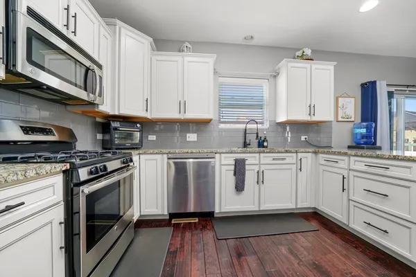 a kitchen with stainless steel appliances granite countertop a stove a sink and white cabinets