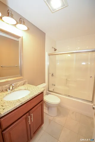 a bathroom with a granite countertop sink a toilet a mirror and bathtub