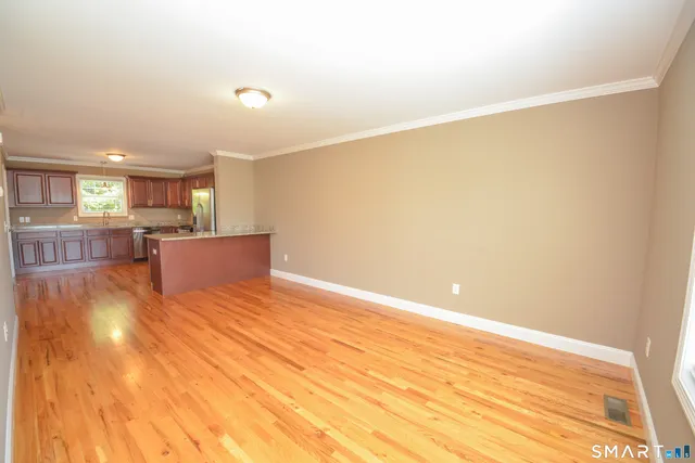 a view of kitchen and empty room with wooden floor
