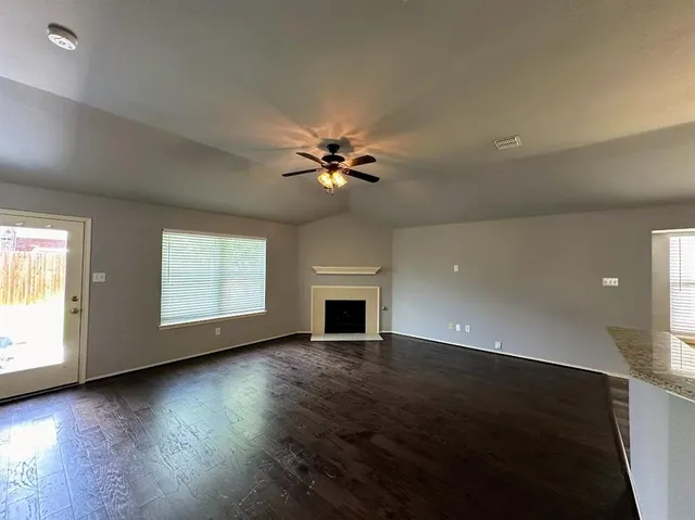 an empty room with wooden floor fireplace and windows