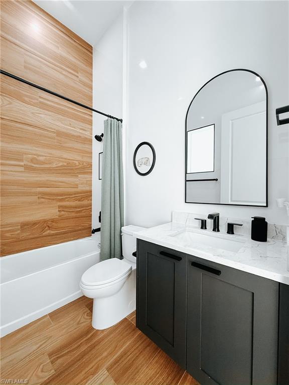 1702 Ludlow Road Marco Island, FL 34145 - Photo 34 of 47 Bathroom featuring wood-finish tile flooring, a dark gray vanity with a white countertop and integrated sink, a contemporary arched mirror, and a shower with wood-finish wall tile