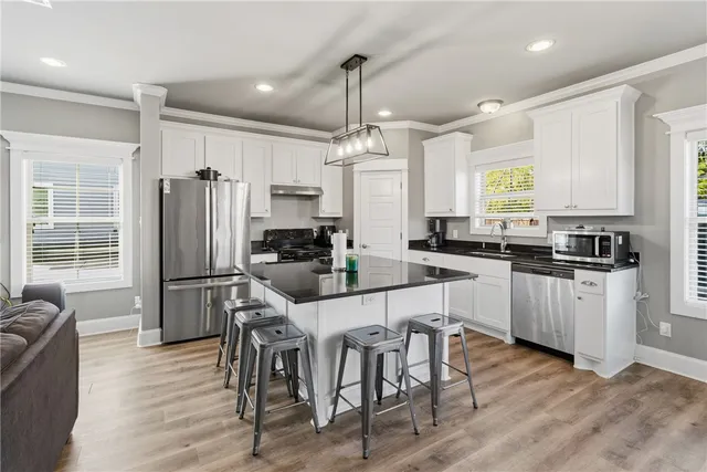 a kitchen with stainless steel appliances granite countertop a refrigerator a stove a sink a dining table and chairs with wooden floor