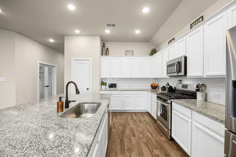 a kitchen with stainless steel appliances granite countertop a sink a stove top oven a refrigerator with white cabinets and granite countertops